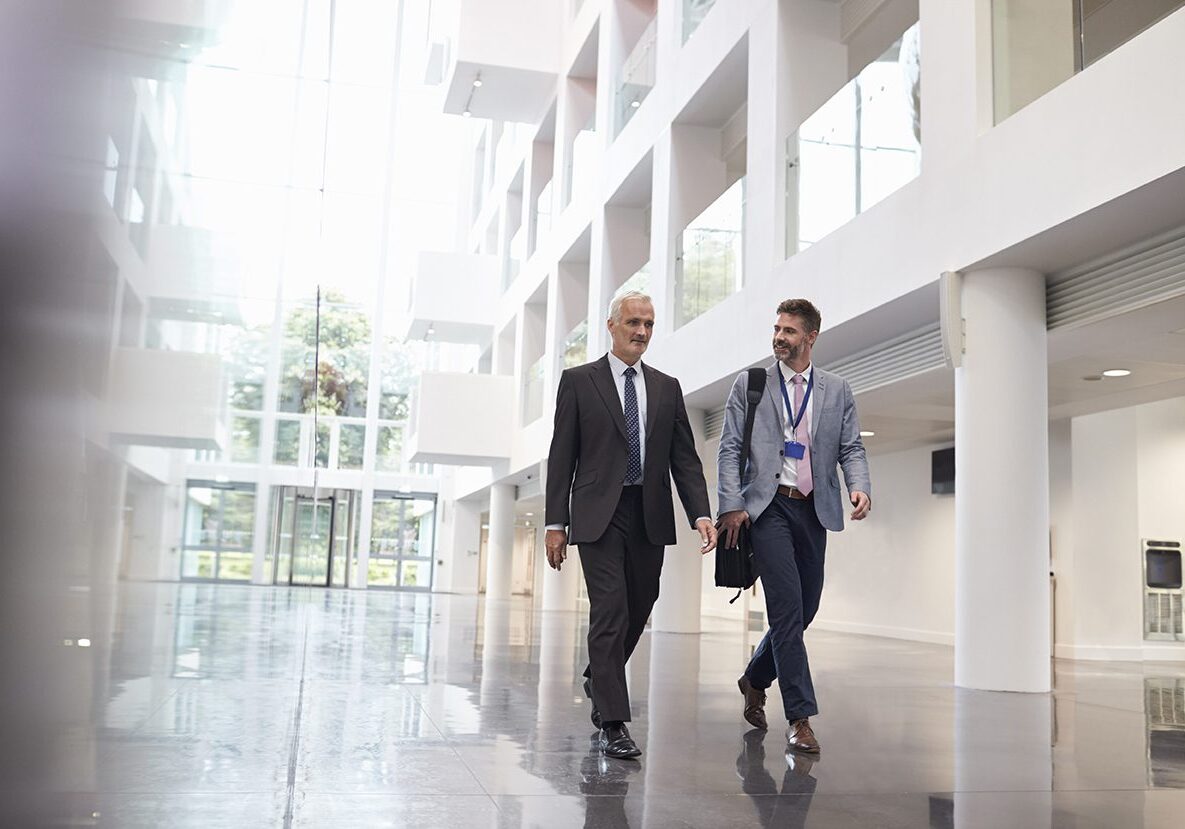 Businessmen Talking As They Walk Through Office Lobby